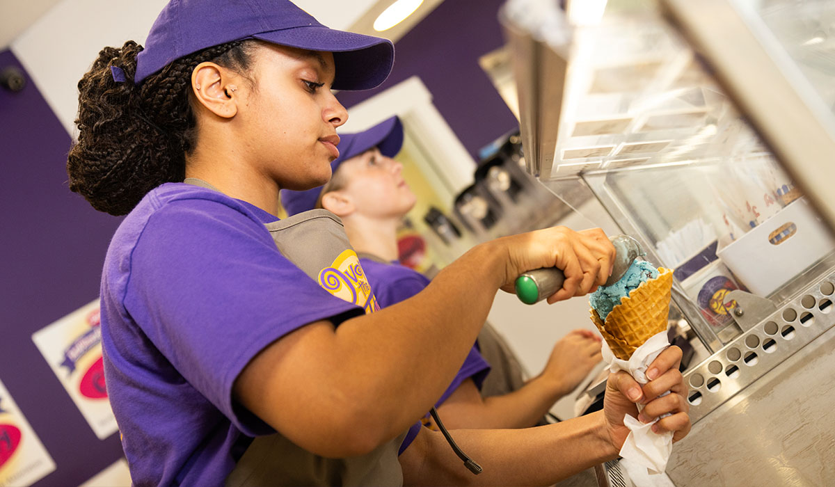 An Over The Top Ice Cream scooper loads a fresh waffle cone with ice cream.