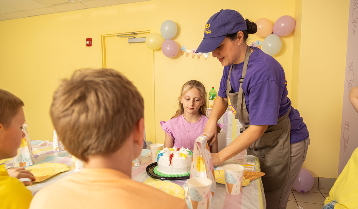 An Over The Top Ice Cream scooper slices ice cream cake to serve to the birthday party guests in the party room.